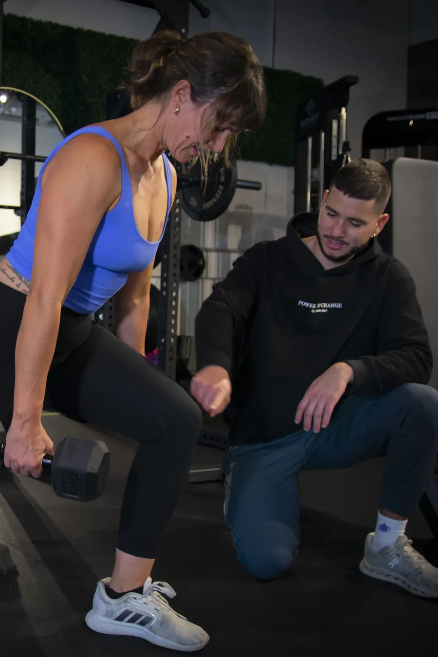 A coach kneeling beside a member, cueing her form on a single-arm dumbbell row during a personal training session at Inside Out Total Wellness in Calgary