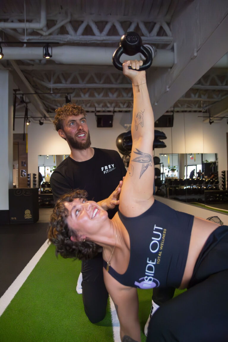 A personal trainer in Calgary coaching a client through a kettlebell workout at Inside Out Total Wellness. The semi-private gym provides expert guidance for strength training and mobility.