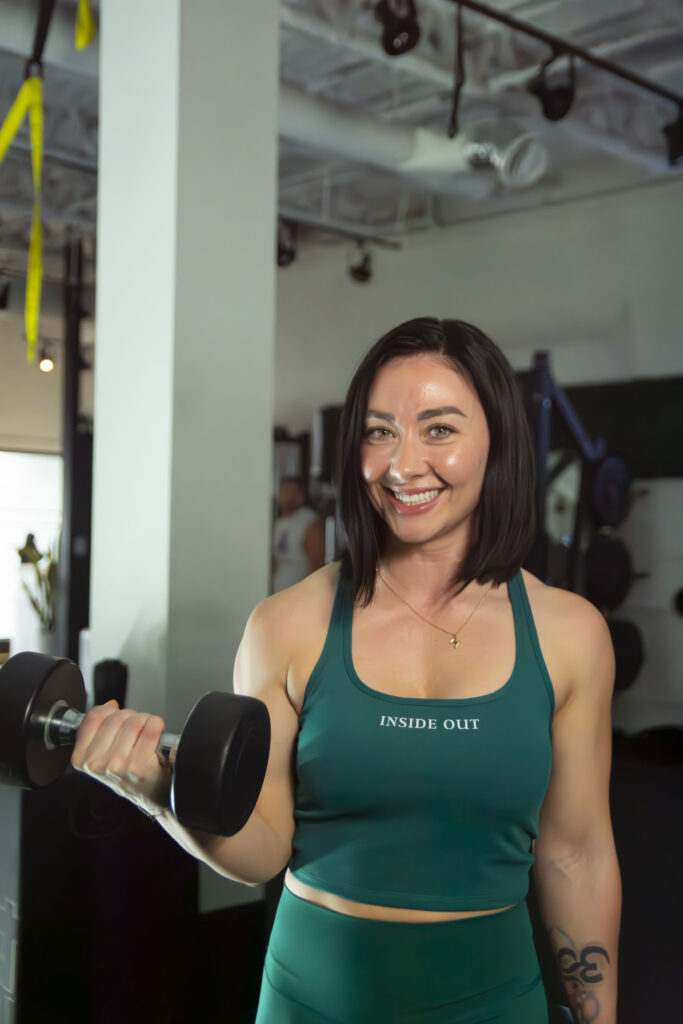 Woman lifting dumbbell and smiling in gym wearing Inside Out activewear